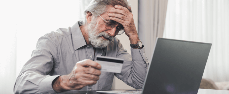 a man holding his credit card in front of a computer looking upset because he was a victim of a elderly financial exploitation in Bradenton & sarasota florida