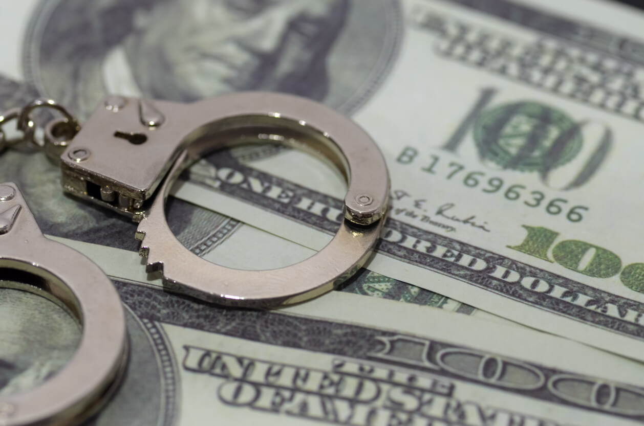 a pair of handcuffs lying on a bed of U.S. dollar bills