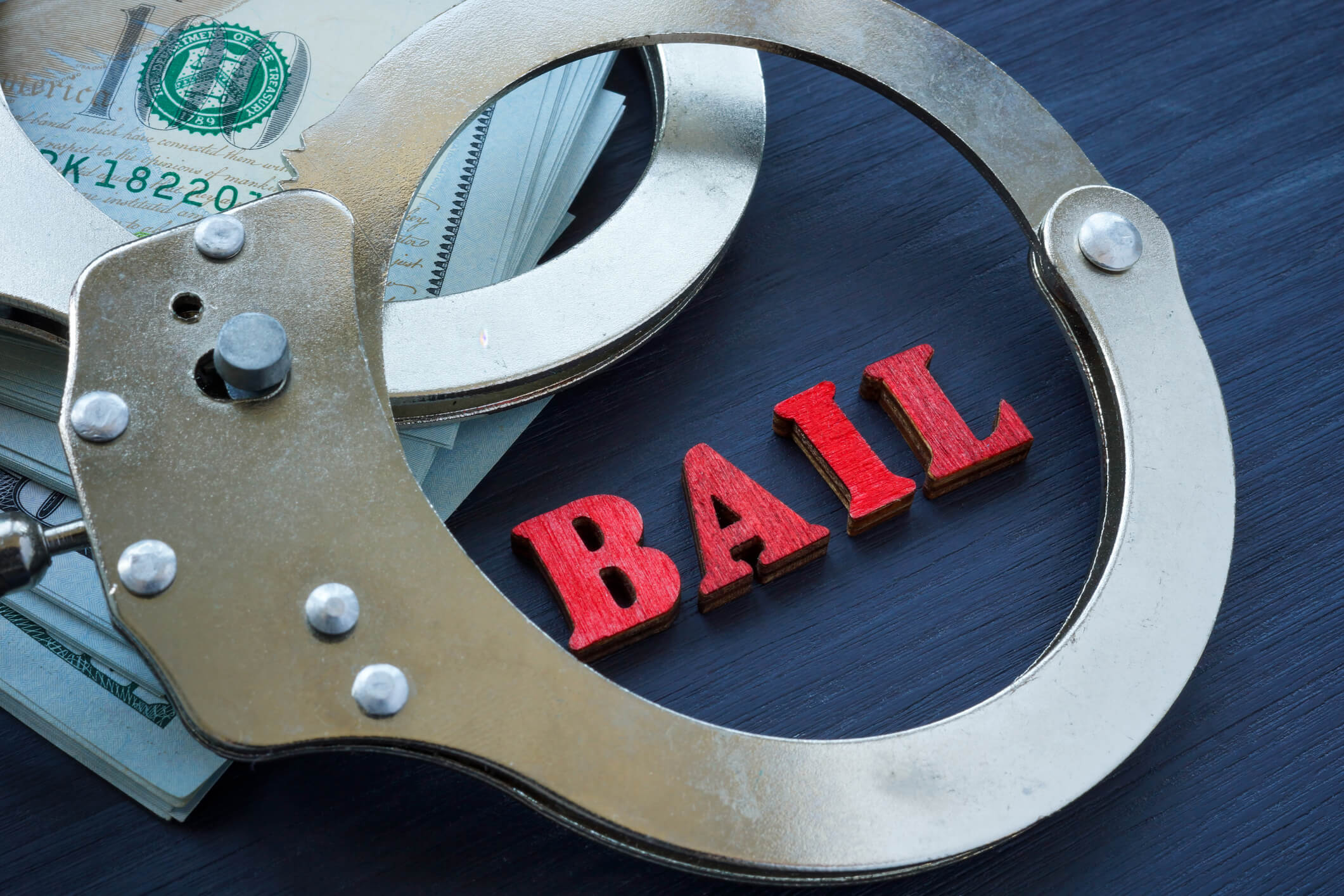 Handcuffs and money with wooden letters spelling BAIL